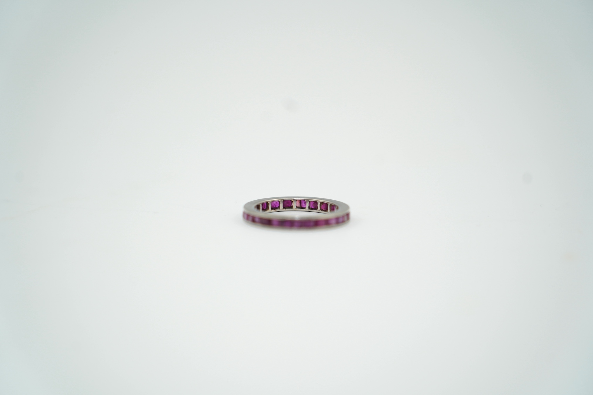 A white metal and rectangular cut ruby set full eternity ring, size M/N, gross weight 3.5 grams. Condition - fair